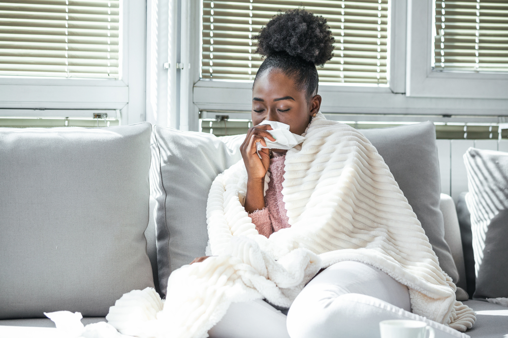 Woman sick with the flu sitting on the couch blowing her nose