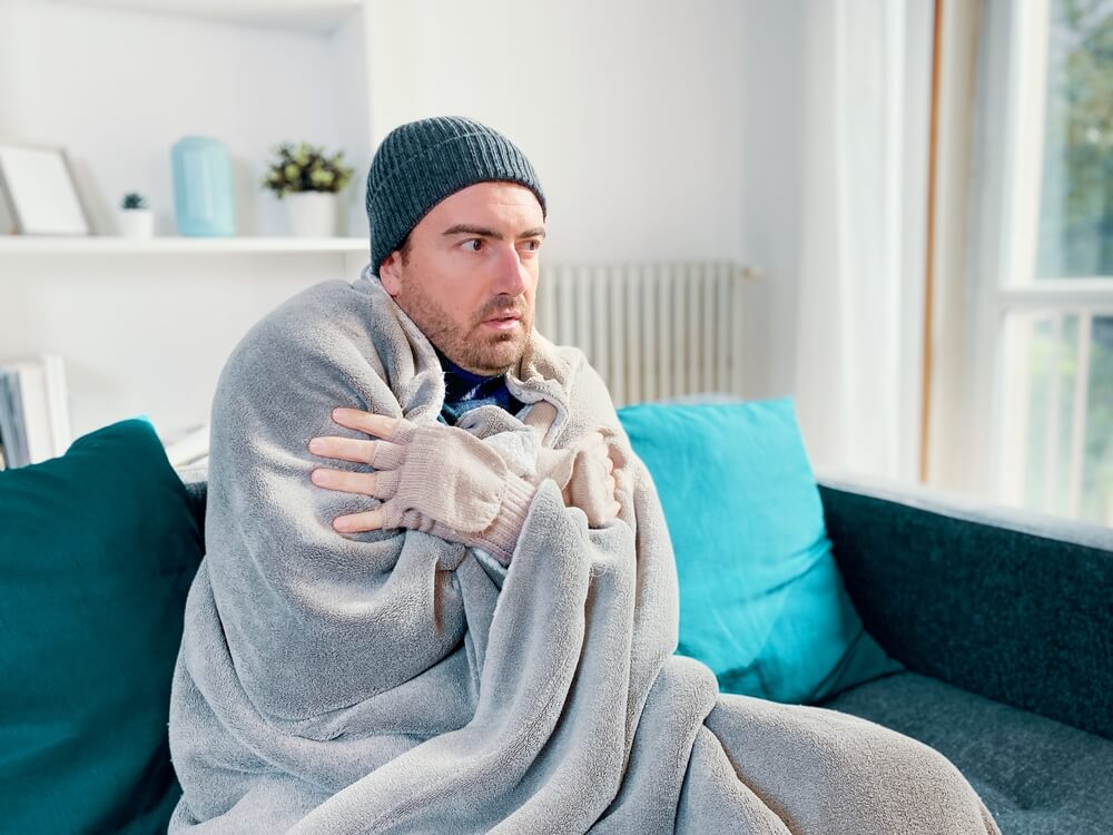 man sitting blanketed in cold home from broken furnace