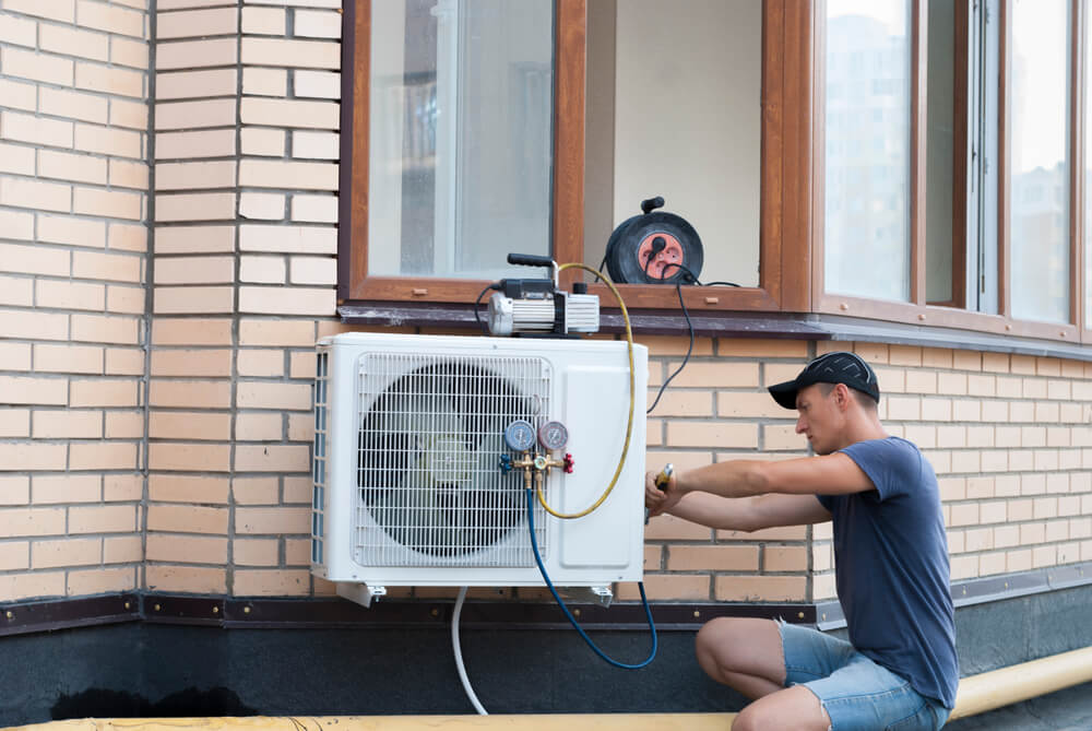 new homeowner squatting while fixing outdoor AC unit with wrench