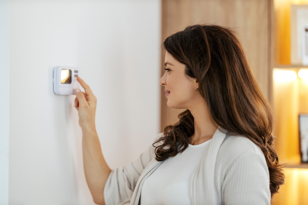 Smiling woman adjusting the thermostat at home